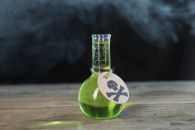 Photo of Flask of poison with warning sign on wooden table against dark background with smoke