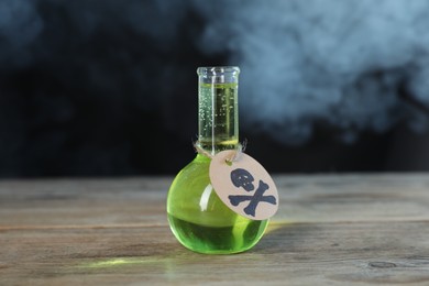Photo of Flask of poison with warning sign on wooden table against dark background with smoke
