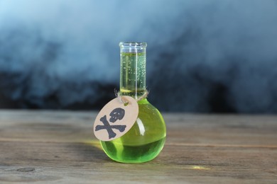Photo of Flask of poison with warning sign on wooden table against dark background with smoke