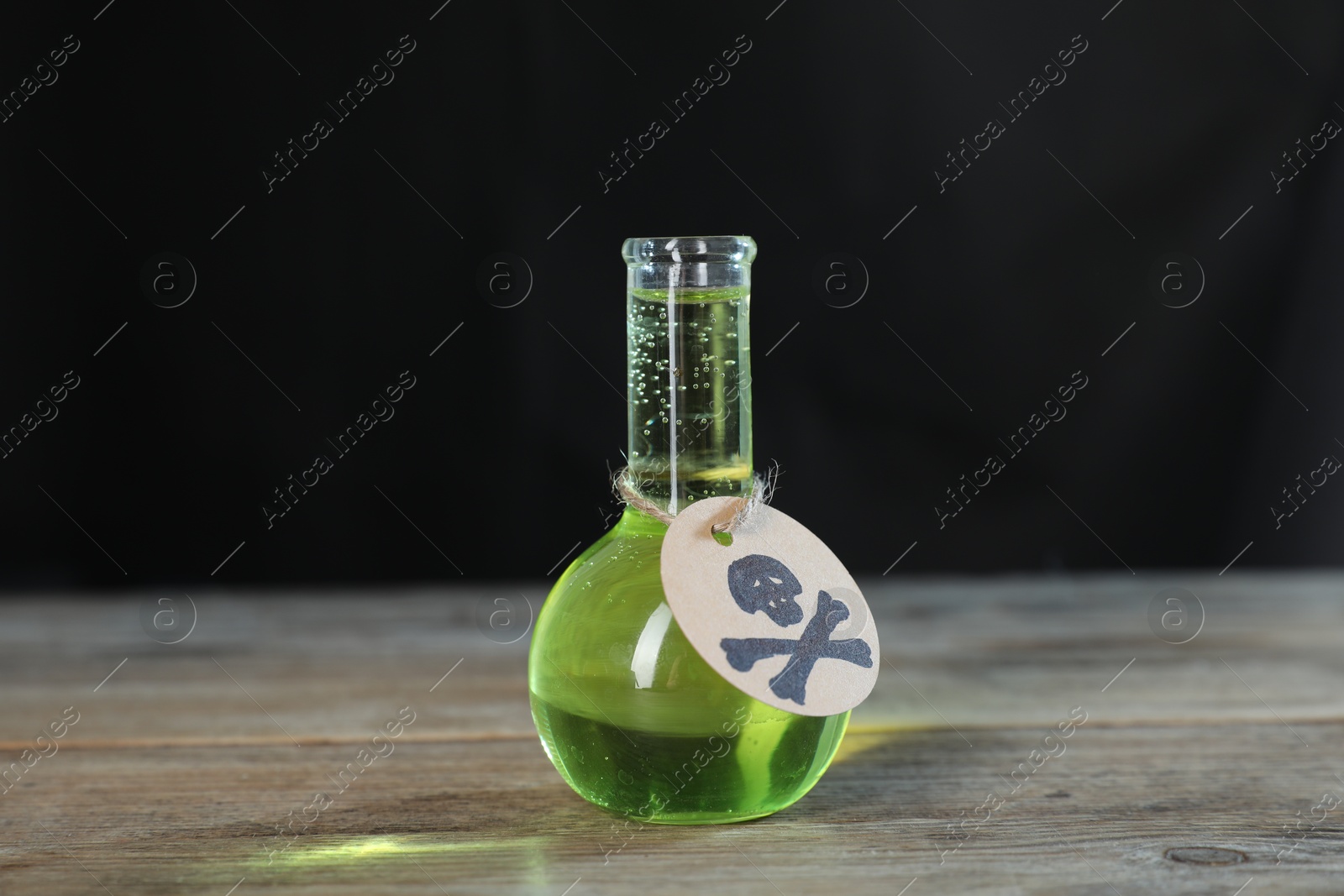 Photo of Flask of poison with warning sign on wooden table against dark background with smoke