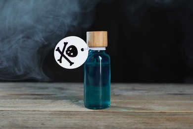 Photo of Bottle of poison with warning sign on wooden table against dark background with smoke