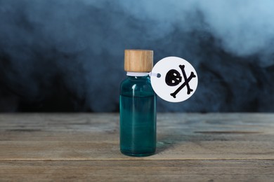 Photo of Bottle of poison with warning sign on wooden table against dark background with smoke