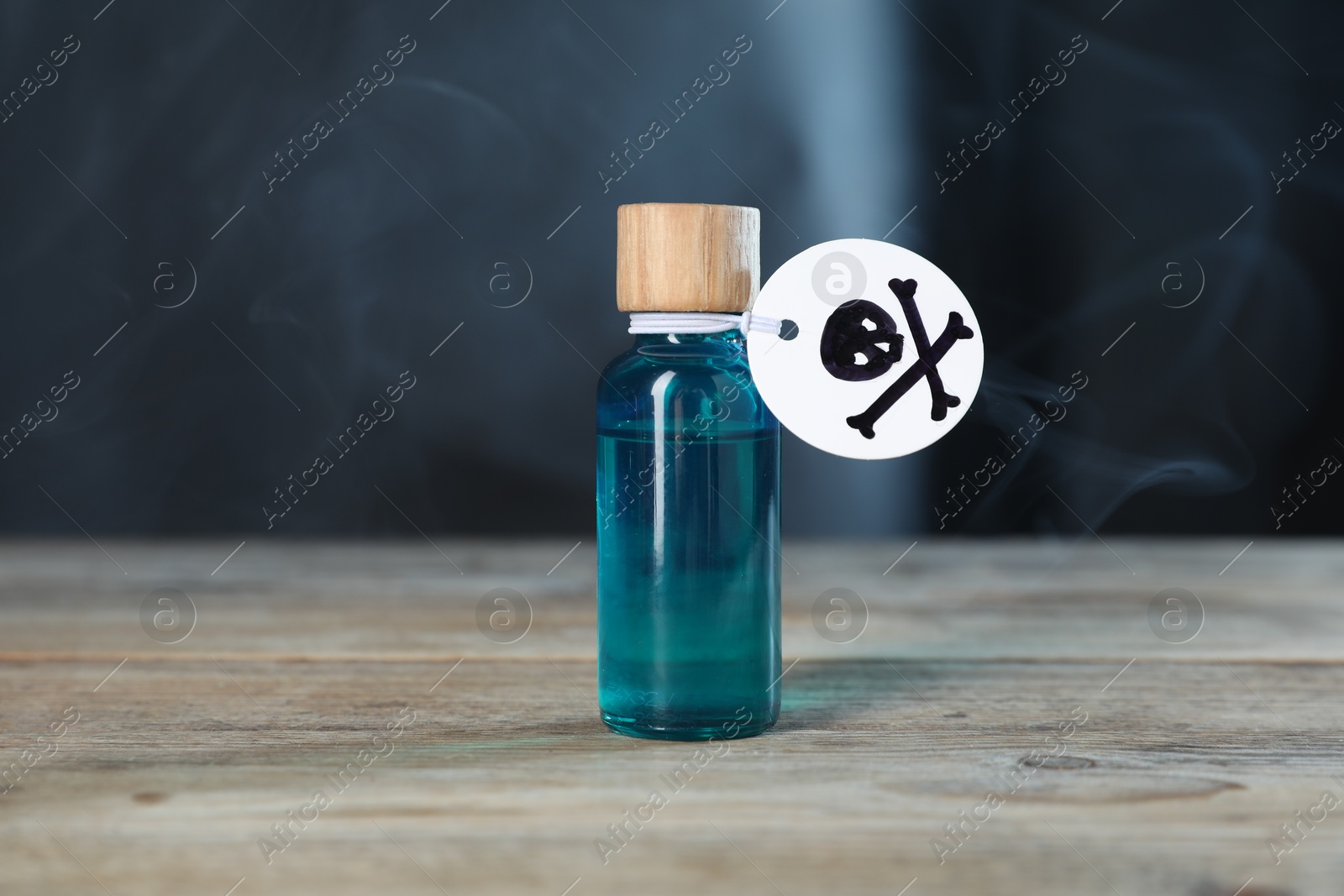 Photo of Bottle of poison with warning sign on wooden table against dark background with smoke