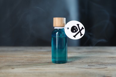 Photo of Bottle of poison with warning sign on wooden table against dark background with smoke