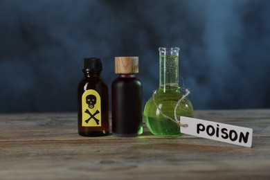 Photo of Bottles of poisons with warning sign on wooden table against dark background with smoke