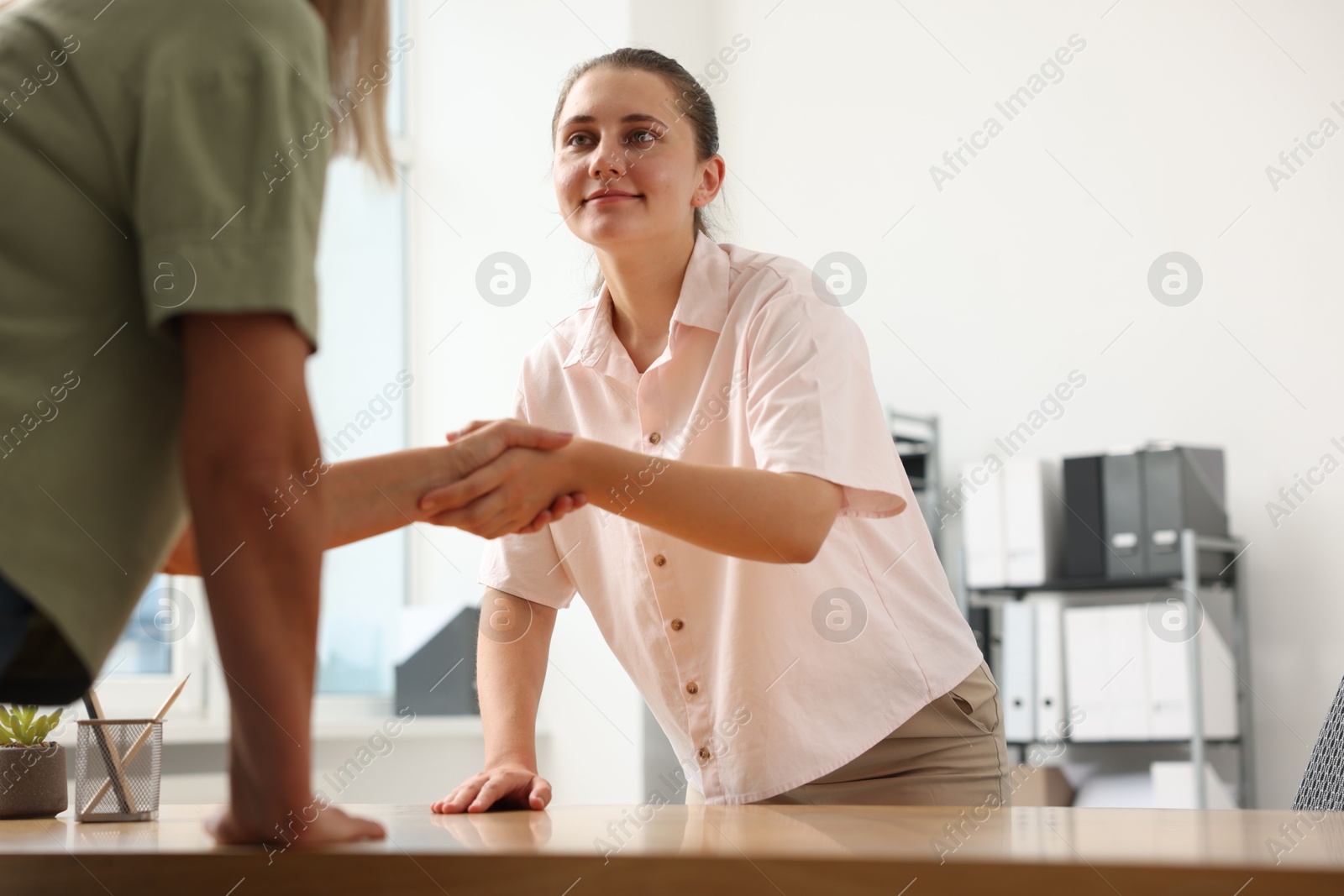 Happy women shaking hands at wooden table in office Photo of Happy women shaking hands at wooden table in office