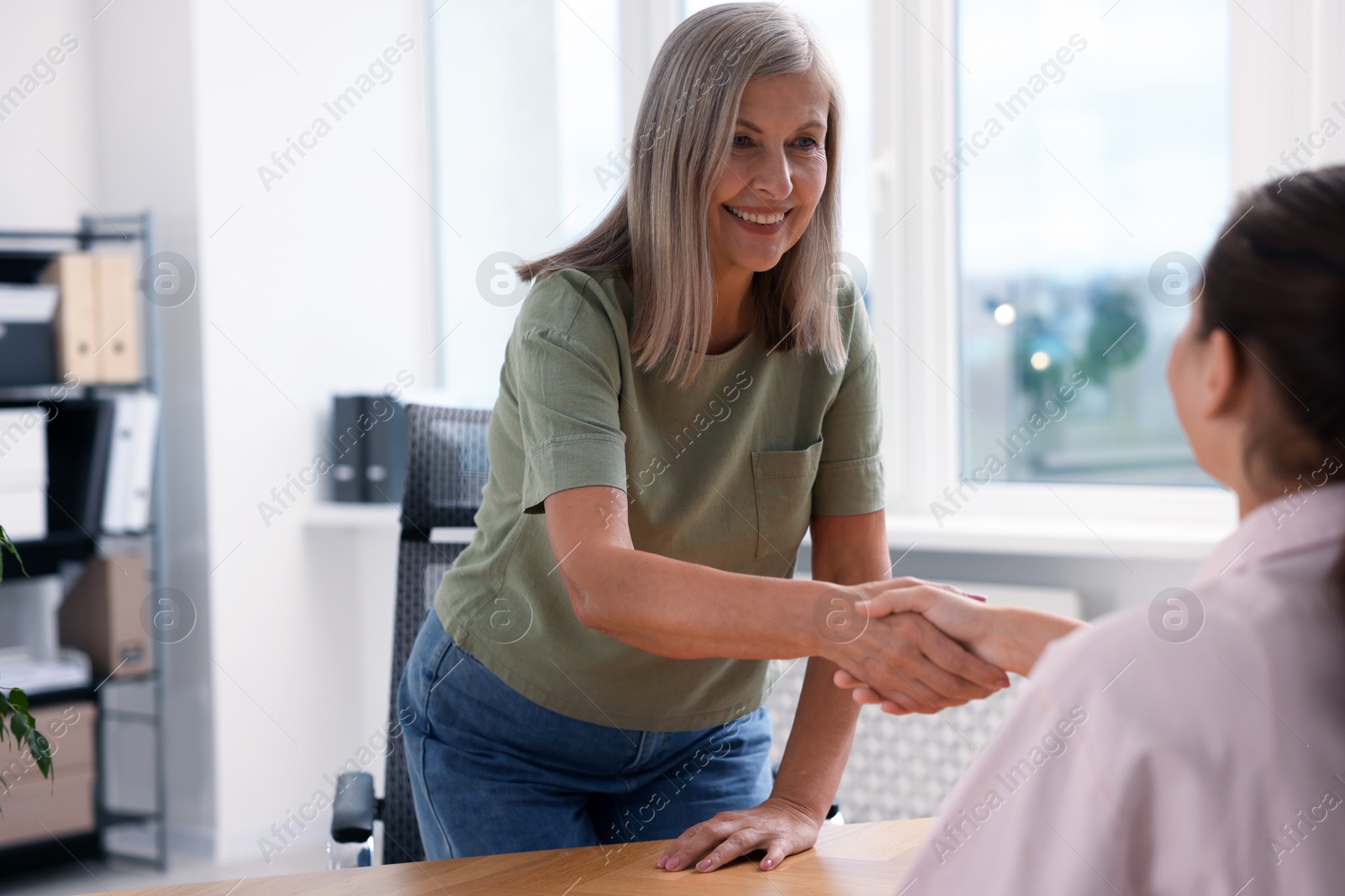 Photo of Happy women shaking hands at wooden table in office