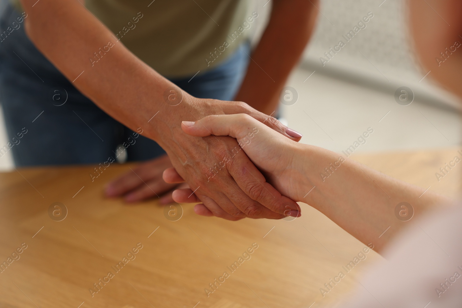 Women shaking hands at wooden table in office, closeup Photo of Women shaking hands at wooden table in office, closeup