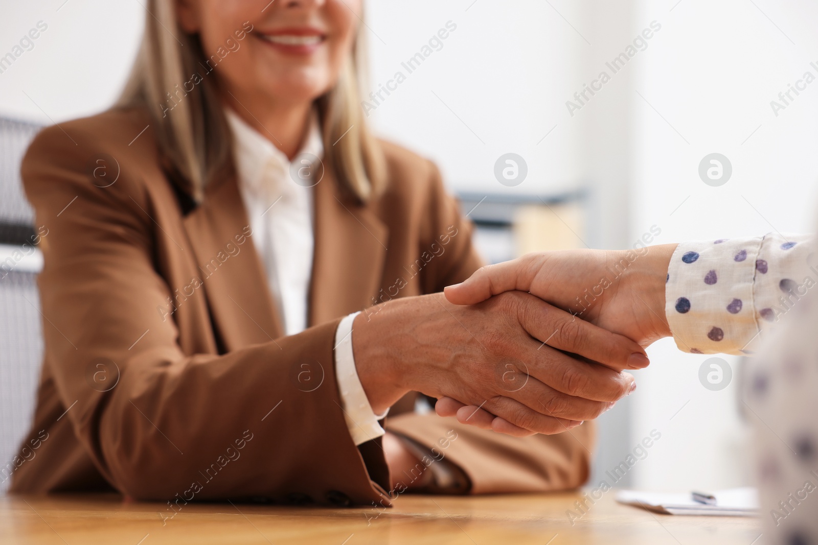 Women shaking hands at wooden table in office, closeup Photo of Women shaking hands at wooden table in office, closeup