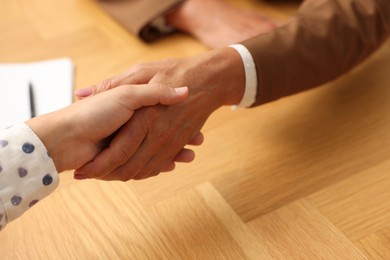 Photo of Women shaking hands at wooden table in office, closeup