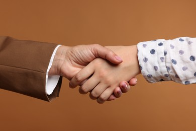 Photo of Women shaking hands on brown background, closeup