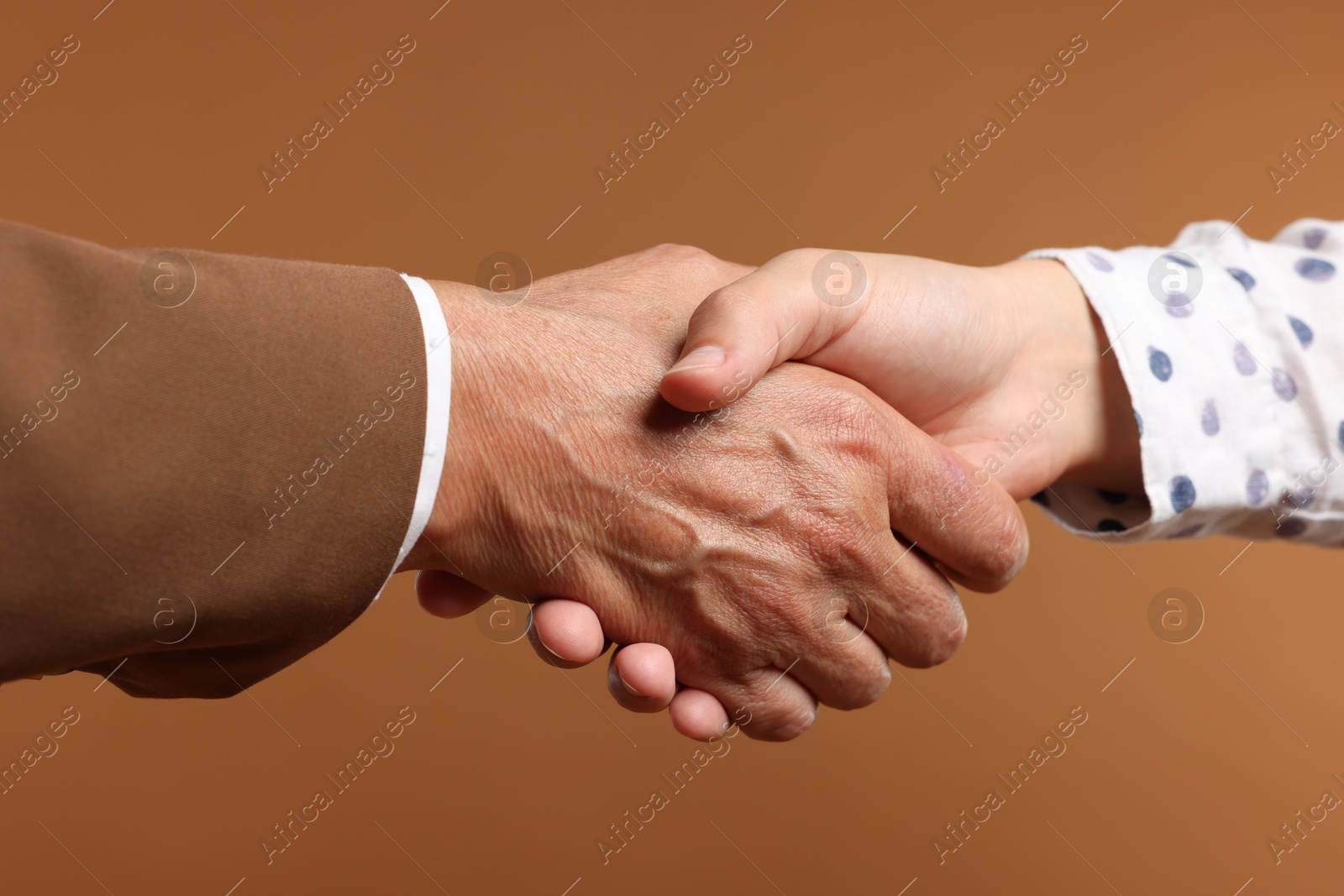 Women shaking hands on brown background, closeup Photo of Women shaking hands on brown background, closeup