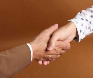 Photo of Women shaking hands on brown background, closeup