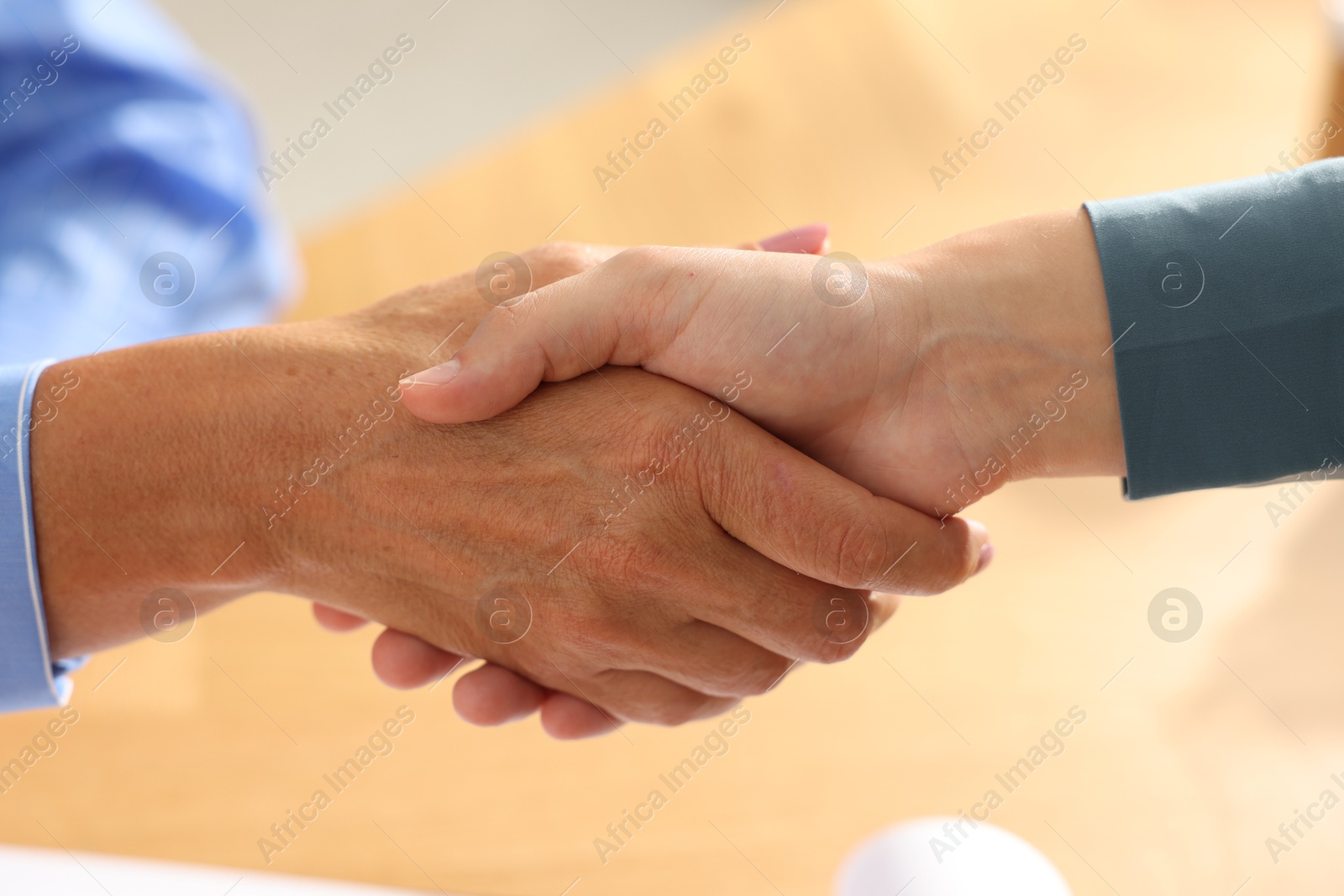Photo of Women shaking hands at wooden table in office, closeup
