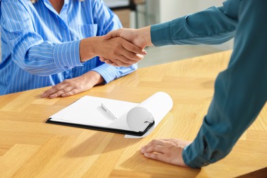 Photo of Women shaking hands at wooden table in office, closeup