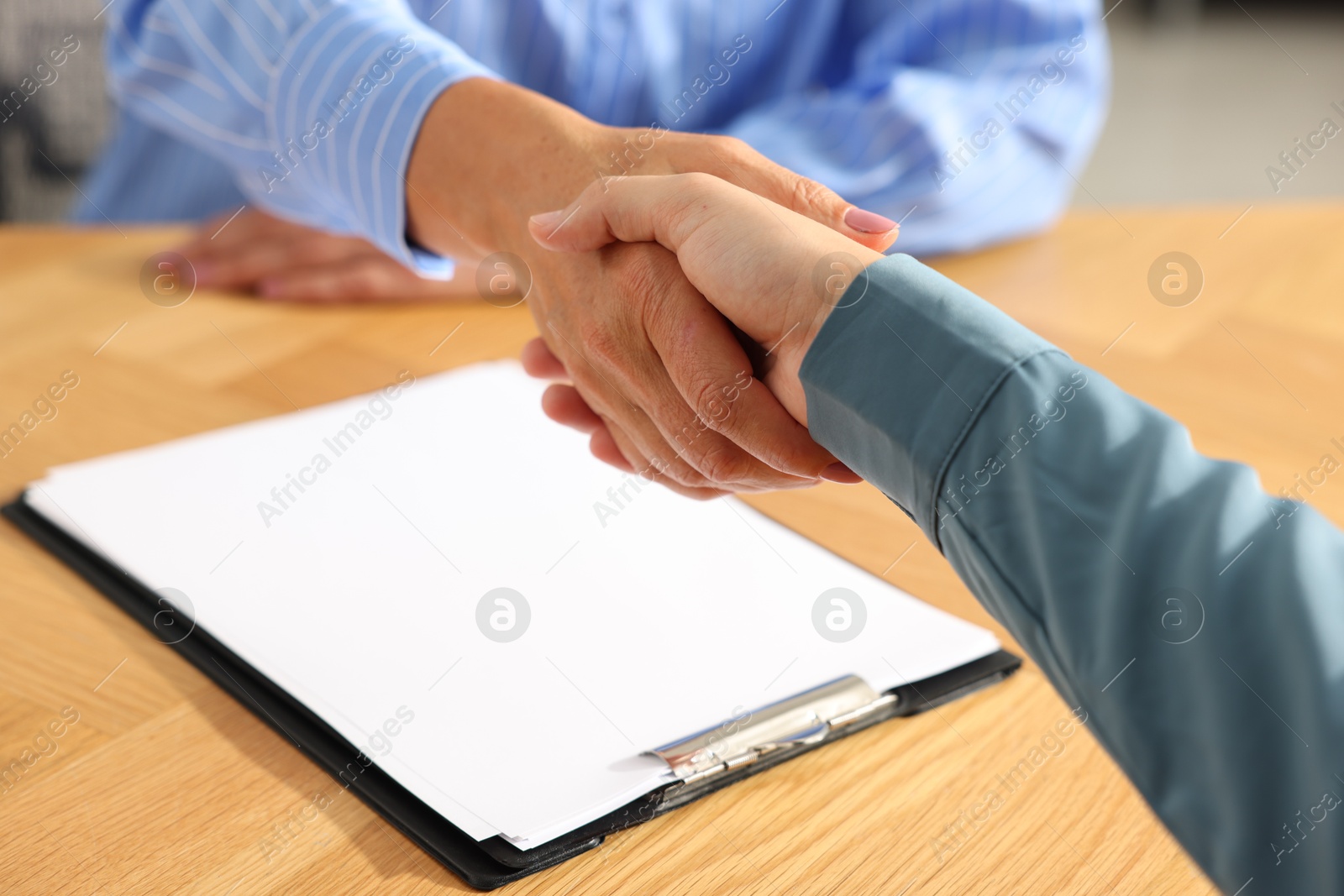 Photo of Women shaking hands at wooden table in office, closeup
