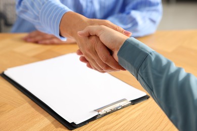 Photo of Women shaking hands at wooden table in office, closeup