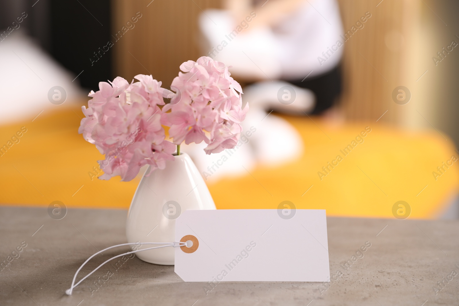Photo of Welcome. Chambermaid making bed in hotel room, focus on blank card and hydrangea flowers