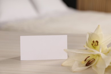 Photo of Welcome. Blank card and beautiful flower on wooden table indoors, closeup