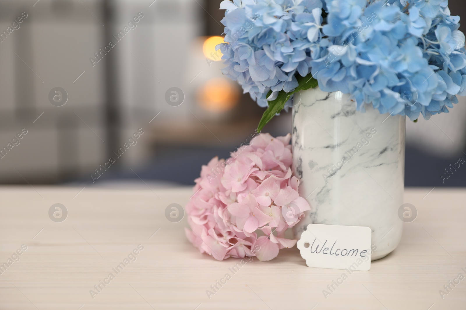 Photo of Card with word Welcome and hydrangea flowers on wooden table, closeup. Space for text