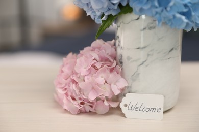 Photo of Card with word Welcome and hydrangea flowers on wooden table, closeup. Space for text