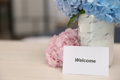 Photo of Card with word Welcome and hydrangea flowers on wooden table, closeup. Space for text