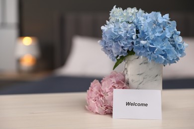 Photo of Card with word Welcome and hydrangea flowers on wooden table, space for text