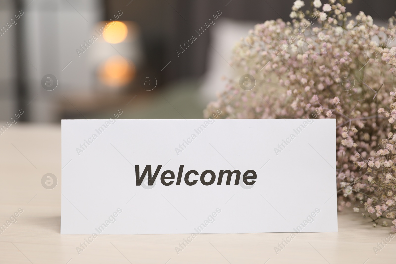Card with word Welcome and gypsophila flowers on wooden table indoors, closeup Photo of Card with word Welcome and gypsophila flowers on wooden table indoors, closeup