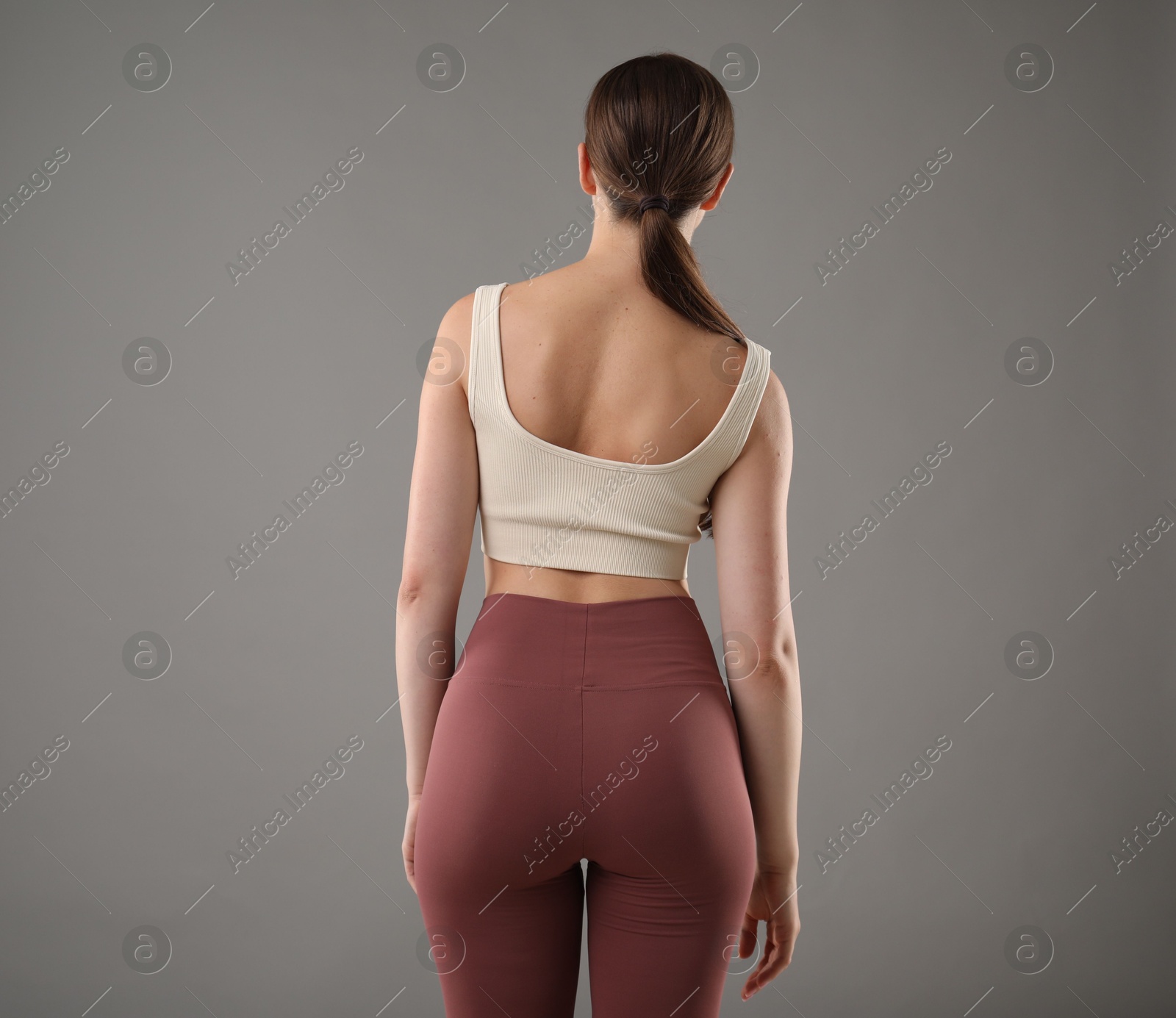 Woman with bad posture on grey background, back view Photo of Woman with bad posture on grey background, back view