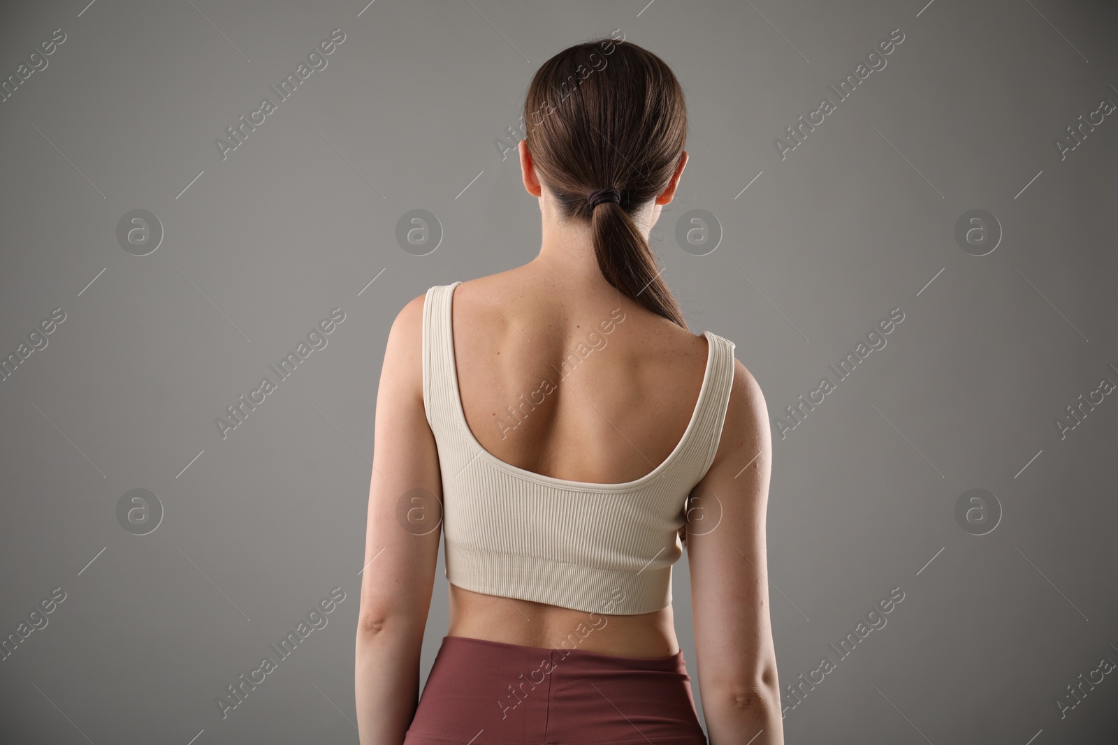 Woman with bad posture on grey background, back view Photo of Woman with bad posture on grey background, back view