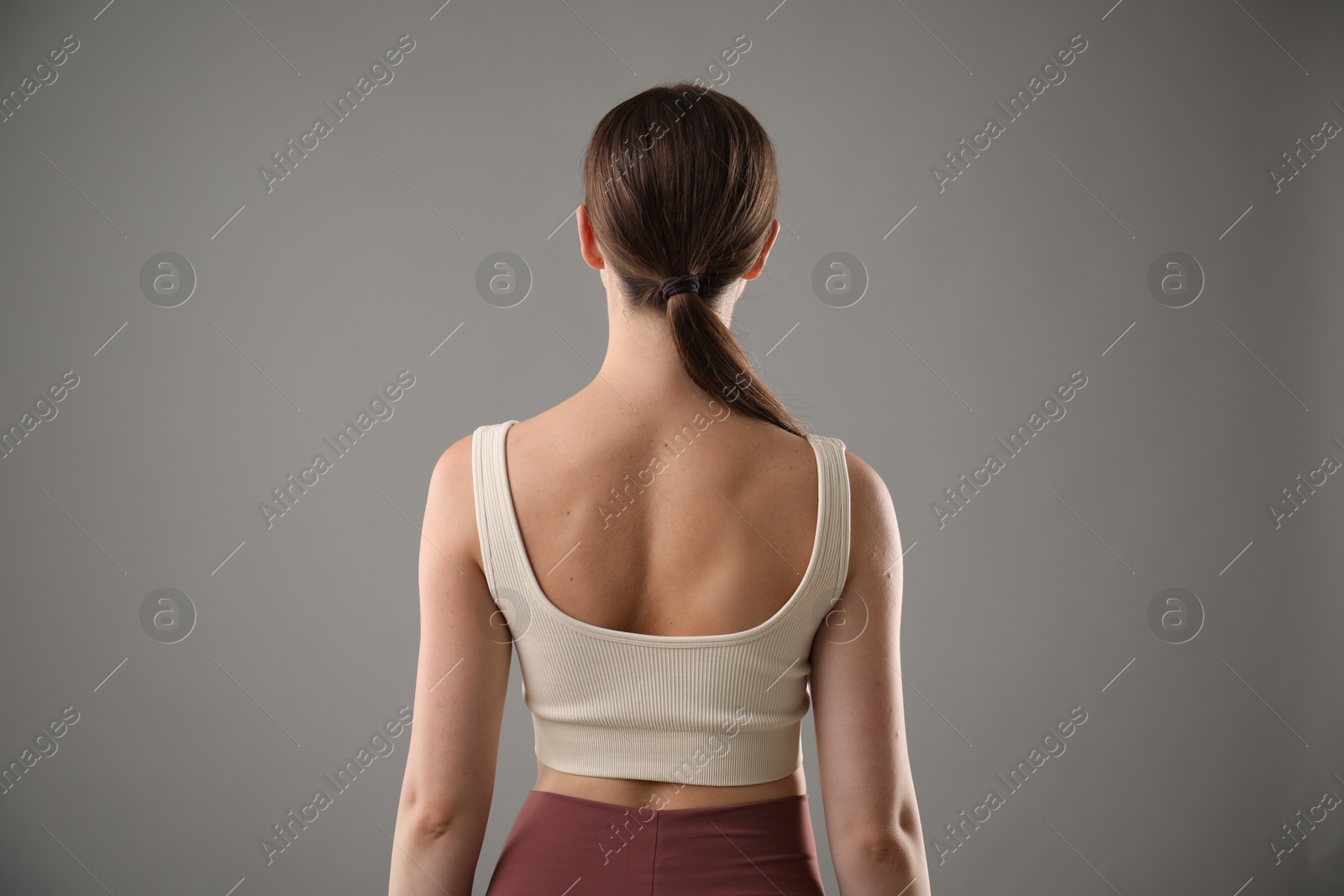Woman with good posture on grey background, back view Photo of Woman with good posture on grey background, back view