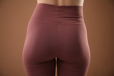 Photo of Woman wearing sports leggings on brown background, closeup