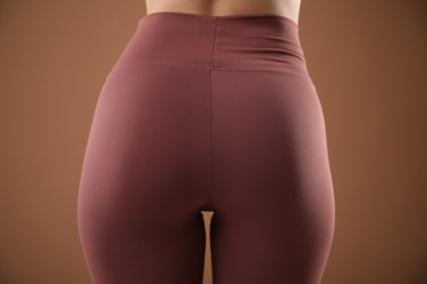 Photo of Woman wearing sports leggings on brown background, closeup