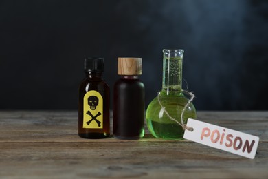 Photo of Bottles of poisons with warning sign on wooden table against dark background with smoke