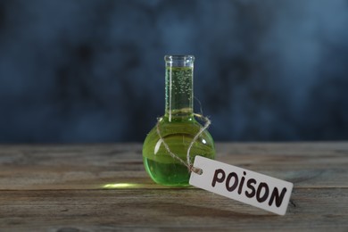 Photo of Flask with poison on wooden table against dark background with smoke