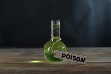 Photo of Flask with poison on wooden table against dark background with smoke