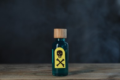 Photo of Bottle of poison with warning sign on wooden table against dark background with smoke