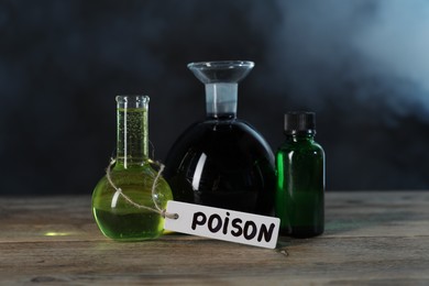 Photo of Bottles with poisons on wooden table against dark background with smoke