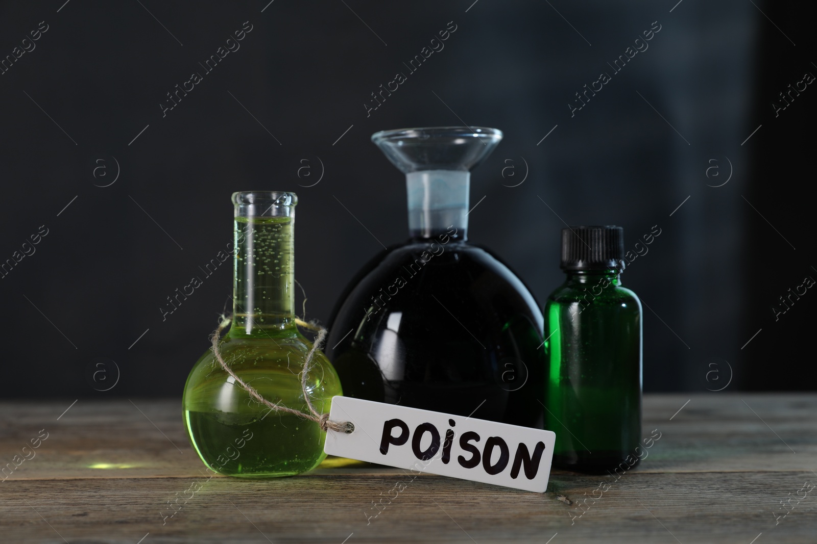 Bottles with poisons on wooden table against dark background Photo of Bottles with poisons on wooden table against dark background