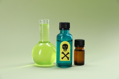 Photo of Bottles of poisons with warning sign on pale olive background