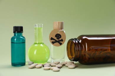 Photo of Bottles of poisons with warning sign on pale olive background, closeup