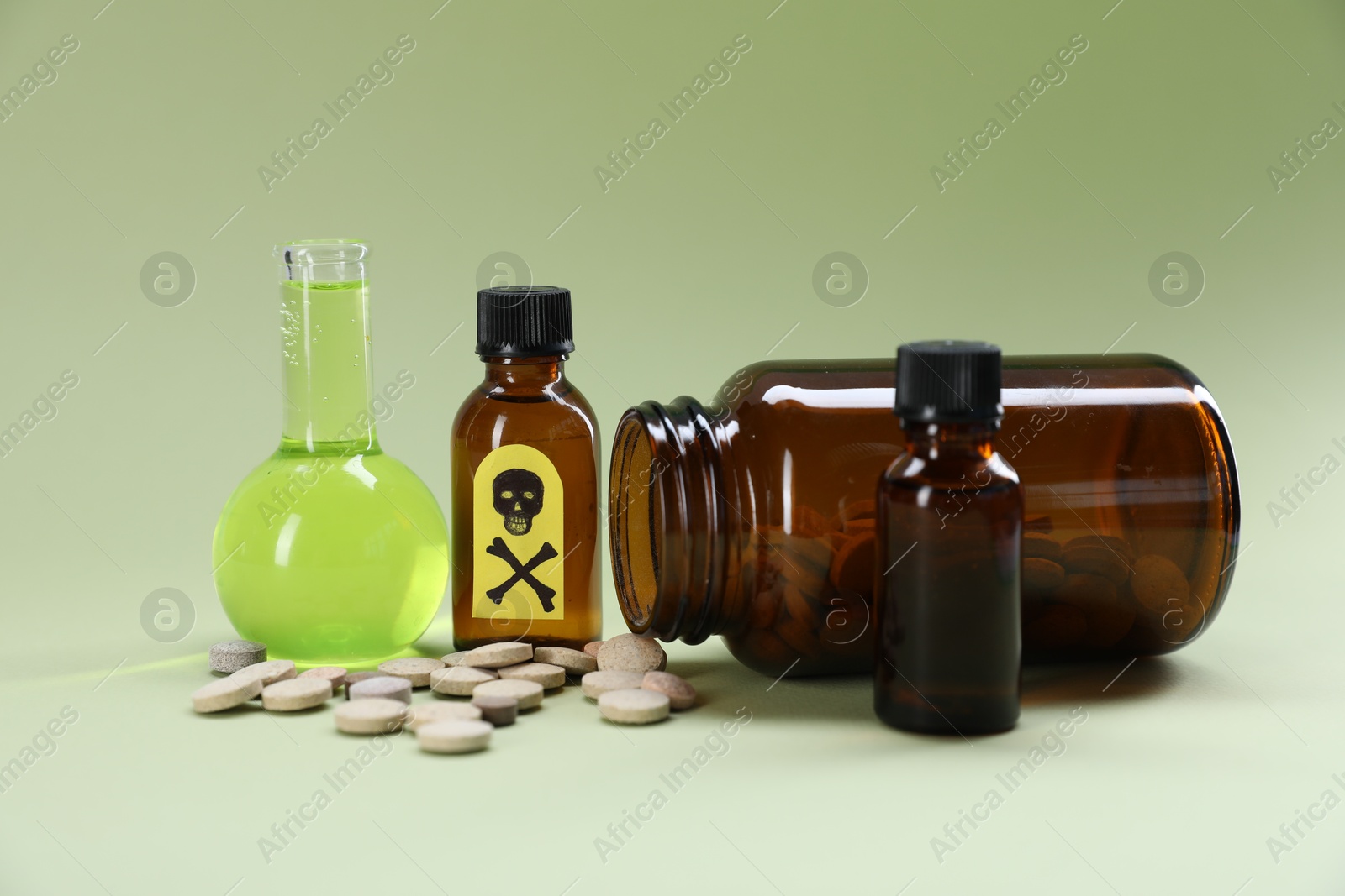 Photo of Bottles of poisons with warning sign on pale olive background