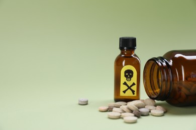 Photo of Bottles of poisons with warning sign on pale olive background, closeup. Space for text