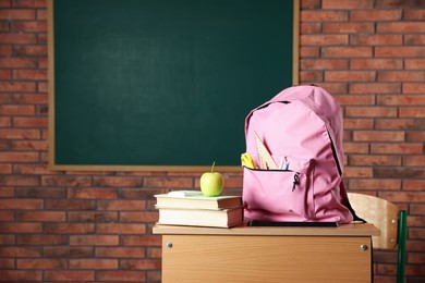 Photo of Pink backpack with different stationery, books and apple on desk in classroom. Space for text