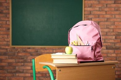 Photo of Pink backpack with different stationery, books and apple on desk in classroom