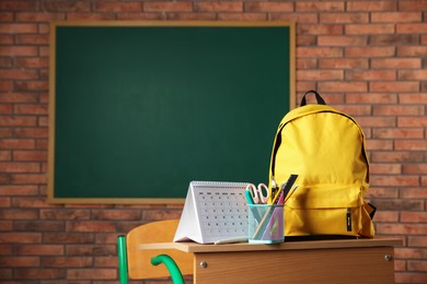 Photo of Yellow backpack, different stationery and calendar on desk in classroom