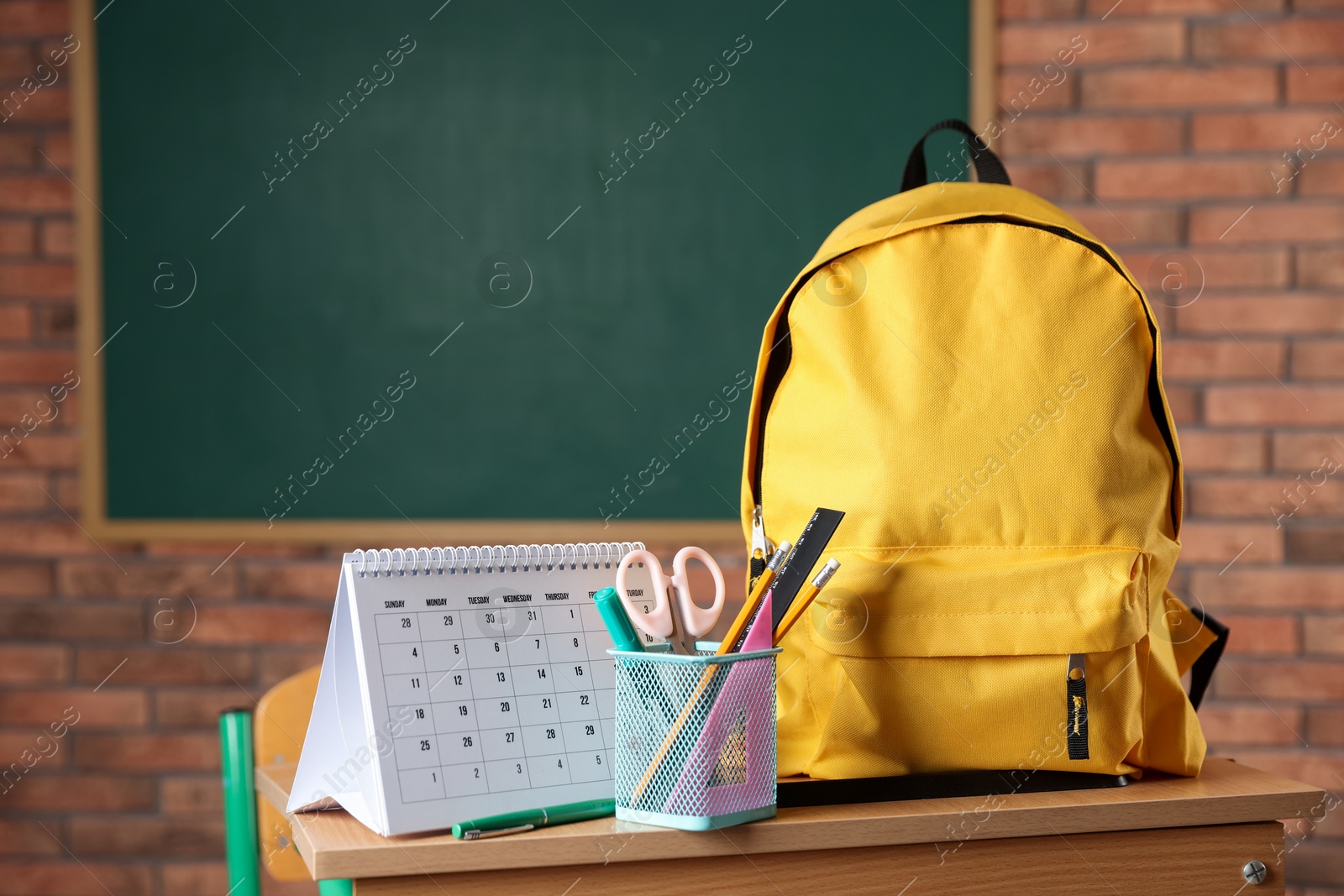 Photo of Yellow backpack, different stationery and calendar on desk in classroom