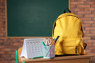 Photo of Yellow backpack, different stationery and calendar on desk in classroom