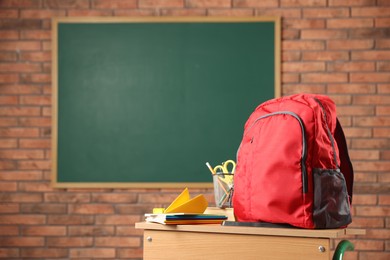 Photo of Red backpack, different stationery and paper plane on desk in classroom. Space for text