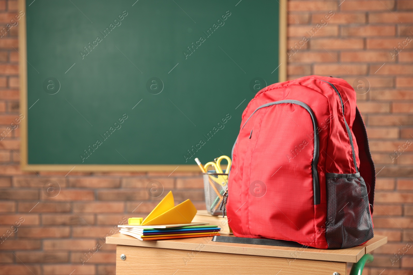 Photo of Red backpack, different stationery and paper plane on desk in classroom